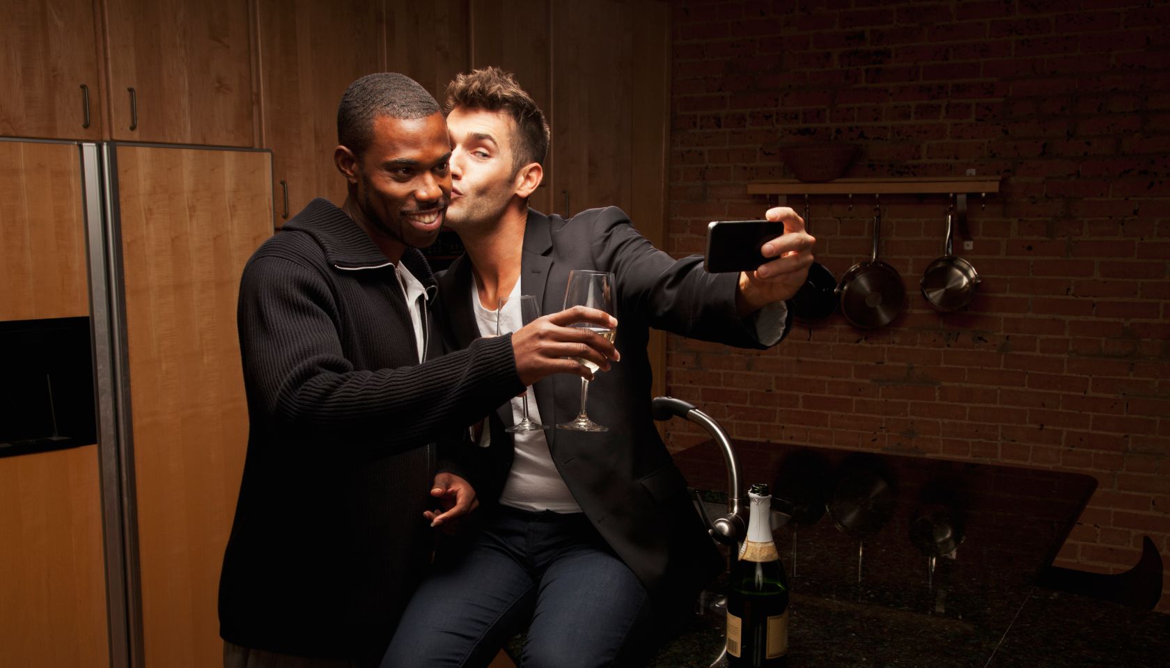 Gay couple drinking wine in kitchen and taking self-portraits