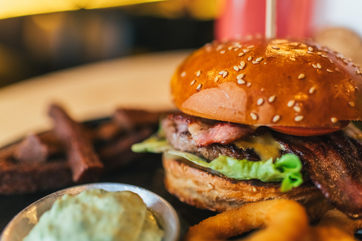 Tasty beef burger with bacon, lettuce, cheese and tomato, onion rings and garlic sauce