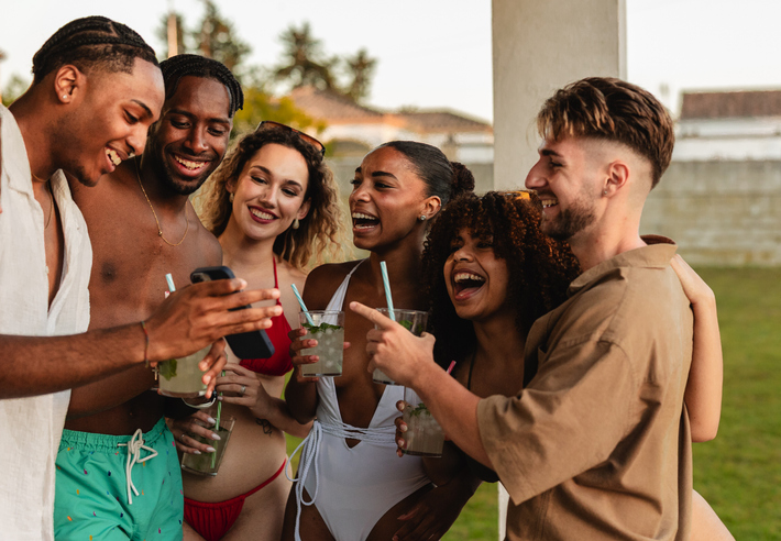 Group of friends laughing together while looking at smartphone at pool party