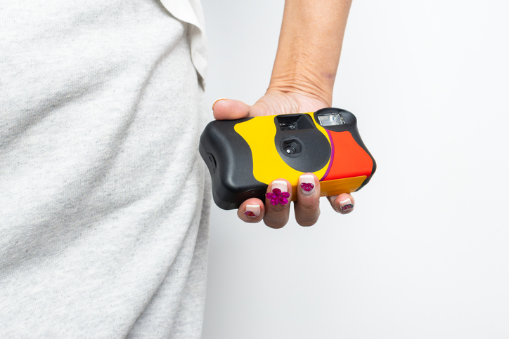 Woman holding colorful disposable camera on white background